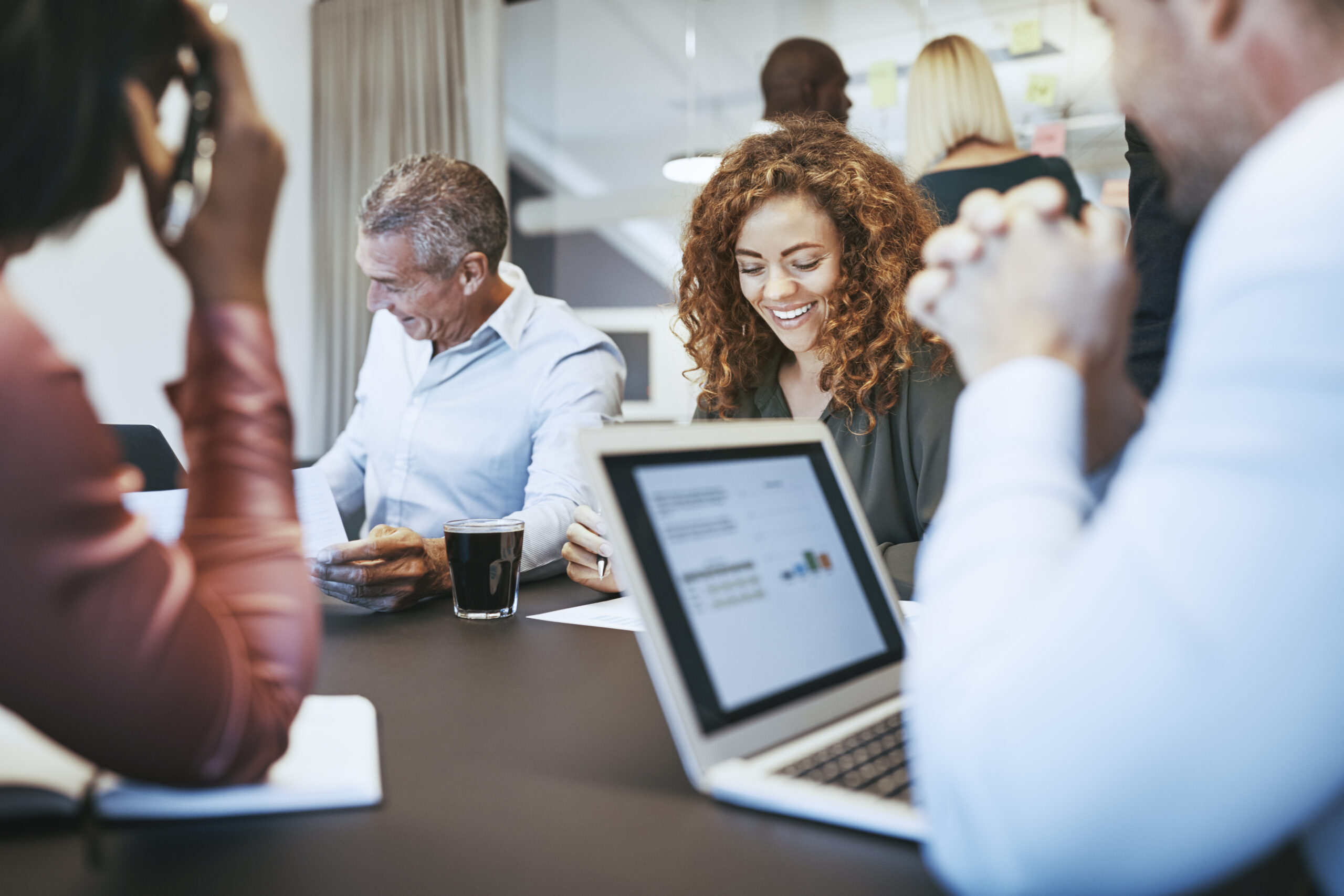 Smiling young businesswoman sitting with a diverse group of work colleagues during a meeting in an office boardroom